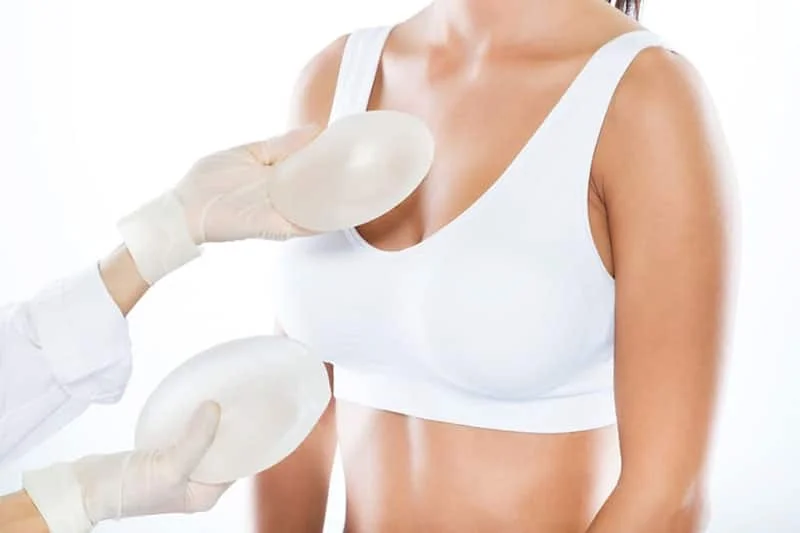 Surgeon holding two silicone breast implants of different sizes beside a patient