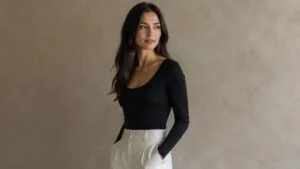 Woman in a black scoop-neck bodysuit standing in profile, showing a natural, proportionate silhouette